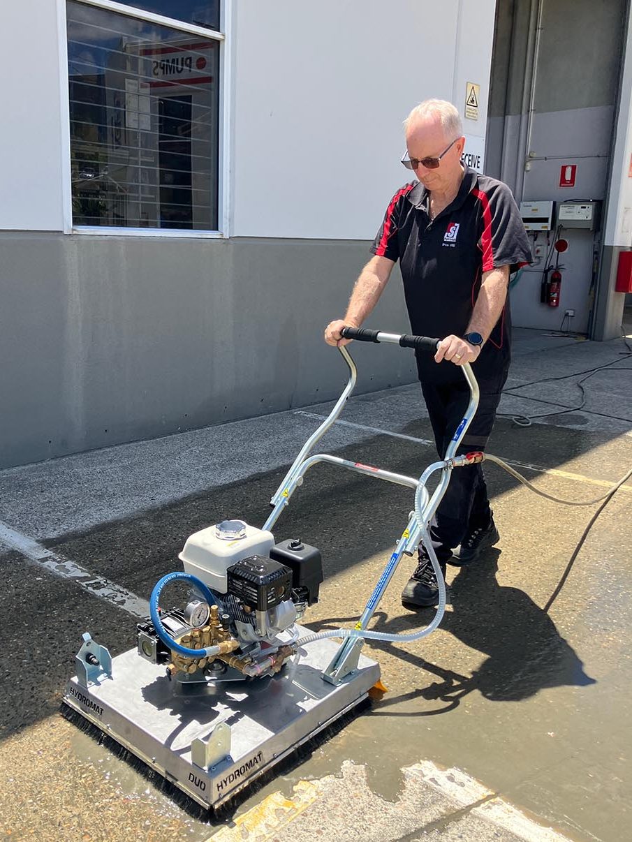 A person using a commercial concrete cleaner on a pavement, demonstrating the equipment in action under sunlight.